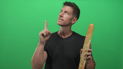 Man pointing finger upward while holding a long baguette in a green studio; playful food marketing idea.