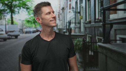 Man smiling and looking up on a city street beside iron railings and parked vans in daylight; confidence ease.