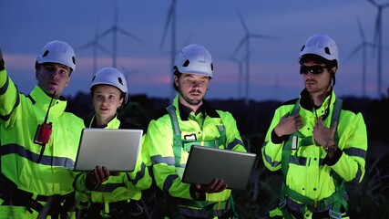 Engineers wearing safety helmets and jackets inspecting a wind turbine at wind farm at dusk. Concept renewable energy, sustainable technology wind power maintenance and environmental engineering. - Powered by Adobe