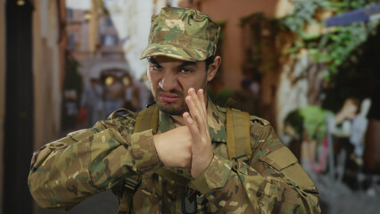 Man in army uniform clenching fist and blocking with palm on old town street lined with stone...