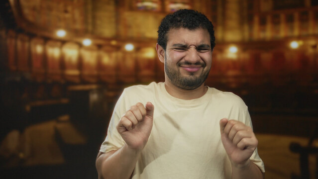 Man with curly hair and beard in beige shirt scrunches face under stained glass windows and wooden pews in church; disgust.
