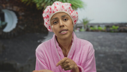 Woman gesturing money request outdoors wearing pink bathrobe and shower cap, suggesting humor and...