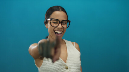 Hispanic woman enthusiastically pointing forward with a joyful expression wearing glasses against a...
