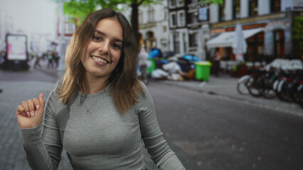 Woman smiling, face forward with raised hands dancing on a cobblestone city street with parked bicycles and outdoor cafe seating; youthful joy.
