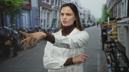 Woman scientist with finger to lips for silence on street wearing white lab coat and turtleneck, pensive gesture; quiet contemplation.