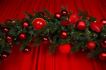 a fragment of a large Christmas wreath decorated with red balls and garlands, on a red satin background with voluminous waves. a podium for New Year's family photo shoots in a photo studio.