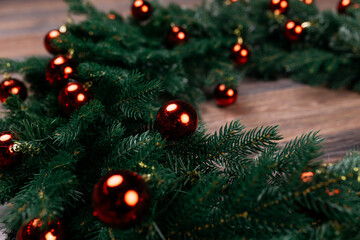 On the dark parquet floor lies a large Christmas wreath made of plastic fir branches with red balls. Delivery service: a wreath made of environmentally friendly materials for interior decoration
