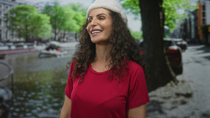 Woman wearing santa hat smiles along canal street lined with green trees and cobblestone buildings;...