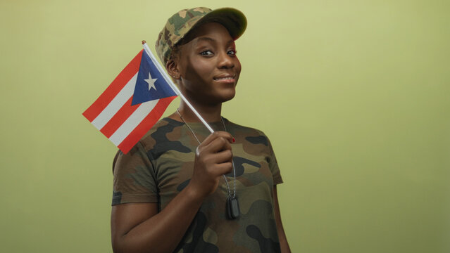 Woman in camouflage uniform holds puerto rico flag and displays dog tags confidently in studio; pride.