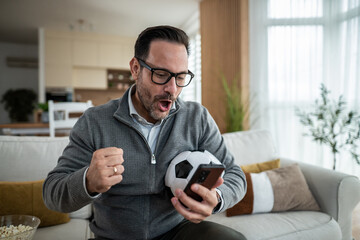 Man watching soccer match and celebrating winning sports bet © Migma_Agency