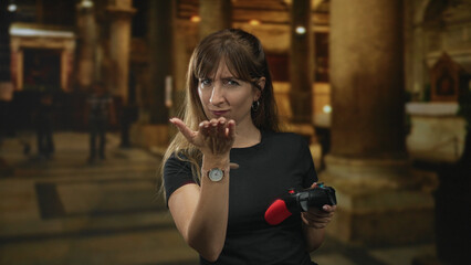 Woman points finger at camera in church while holding red game controller and wearing wristwatch; challenge defiance.