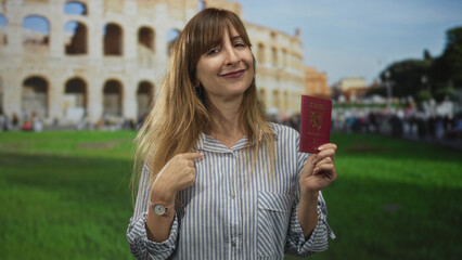 Woman holding passport and pointing finger to passport in front of roman coliseum building with a...