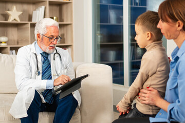 Fototapeta premium Visit to pediatrician doctor. Mother with little preschooler son visit consult male pediatrician at hospital. Doctor examining boy. Family and doctor have consultation in doctor office clinic at home
