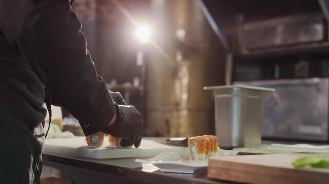 Cinematic close up shot of unrecognizable male chef carefully plating salmon sushi roll preparing for serving in professional restaurant kitchen, copy space - Powered by Adobe
