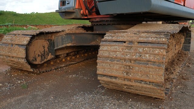Close-up of an excavator wheel covered in thick red mud at a construction site, showing heavy machinery, rugged terrain, earthmoving work, dirt, and challenging ground conditions.