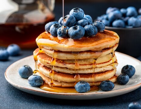 fluffy pancakes stacked high drizzled with syrup and topped with fresh blueberries