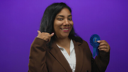 Woman holding a blue first place ribbon and making call me gesture in purple studio; confidence...