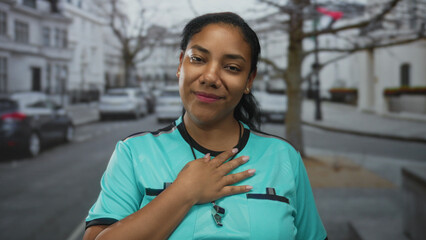 Woman referee wearing turquoise uniform smiling with hand on chest on street; pride trust dedication.