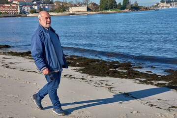 Elderly man walking by the sea on a sunny day in a relaxed, natural setting
