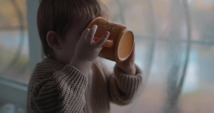 A little boy drinking tea sitting on the windowsill at the autumn day. Video contains original audio.