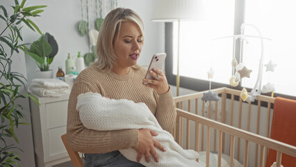 Woman holds swaddled baby near crib in bedroom while gently holding phone to ear; motherhood responsibility.