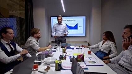 A diverse team of business professionals engages in a productive meeting, with a presenter discussing data analysis displayed on a screen. - Powered by Adobe