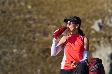 Athlete taking a break to hydrate with water bottle during hiking in mountainous terrain on a sunny day