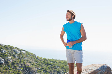 Man standing on rocky coastal hillside holding blue water bottle and wearing blue shirt, copy space