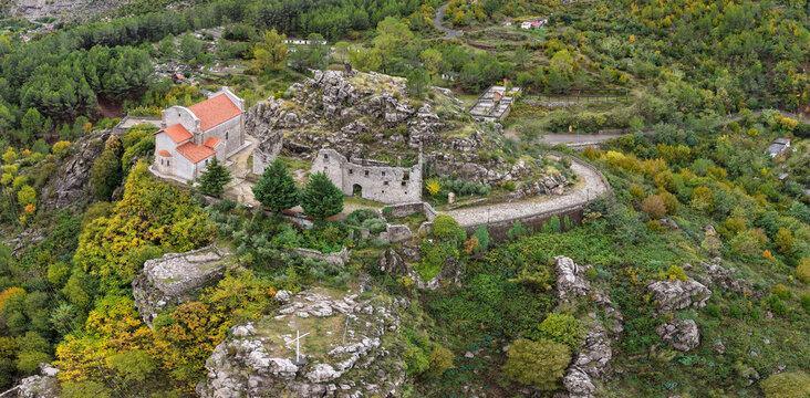 Aerial close view of Rubik Monastery and its stone ruins perched on rugged cliffs surrounded by colourful autumn vegetation.