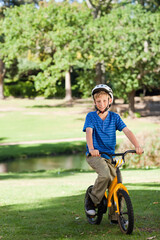 Child male riding yellow bicycle wearing white helmet and blue striped shirt near small pond