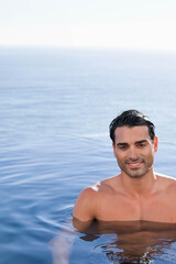 Mid-adult man standing chest-deep shirtless in calm blue sea with ripples and droplets, copy space