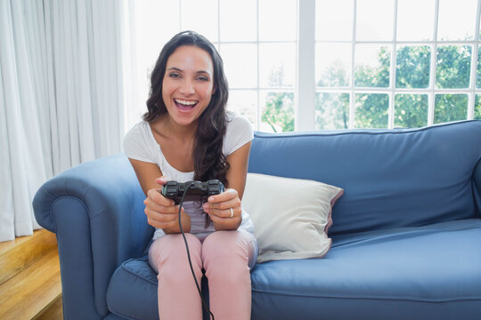 Female sitting on blue sofa in living room in white top pink pants holding wired controller