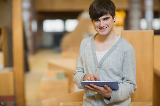 Adult male standing near bench backrest holding tablet tapping screen in warm library, copy space