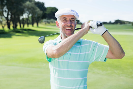 Senior man standing on fairway holding driver across shoulders, wearing striped polo, white glove - Powered by Adobe