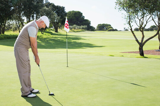 Mature man preparing to putt on putting green, holding putter and eyeing golf ball