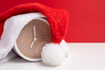 Alarm clock covered with santa hat on red and white background. Holiday Countdown.
