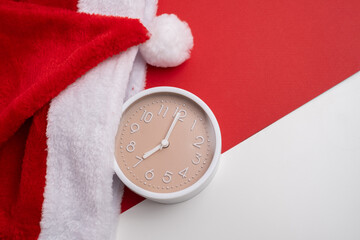 Alarm clock covered with santa hat on red and white background. Holiday Countdown.