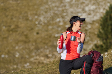 Fototapeta premium Woman enjoying a warm drink while resting on a hiking trail in the mountains during a sunny day
