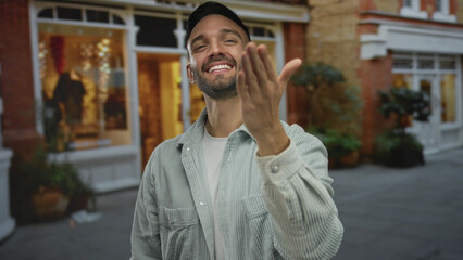 Young man smiling on urban street outdoors invitingly with hand extended wearing casual shirt near shopfront at night capturing warm city ambiance for lifestyle imagery