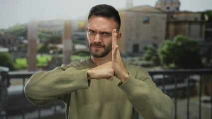 Hispanic man in a green sweater making a determined gesture of striking his palm with his fist, set against the backdrop of ancient roman ruins in italy, showcasing cultural heritage. © Krakenimages.com
