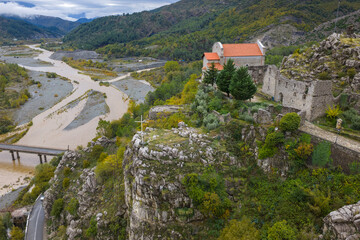 Aerial view of Rubik Monastery and stone ruins above the river, perched on rugged cliffs surrounded by rich autumn colours.
