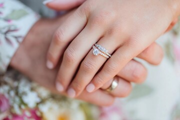 Couple's hands showing wedding and engagement rings with floral background during a romantic moment in nature