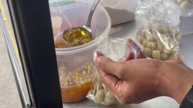 Video vendor adding chili powder, garlic oil, and salt to cimol street food.