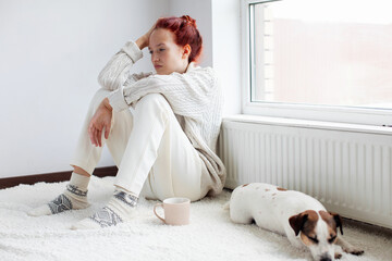Sad young Woman sitting near radiator at home
