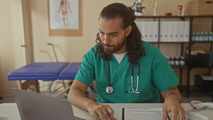 Man doctor with stethoscope typing on laptop in clinic while reviewing patient form and gesturing toward screen; focus.