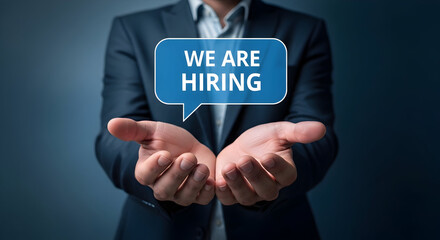 Man in suit holding "We are Hiring" speech bubble showcasing recruitment and job opportunities for career growth and employment in the business sector attracting talent and new employees