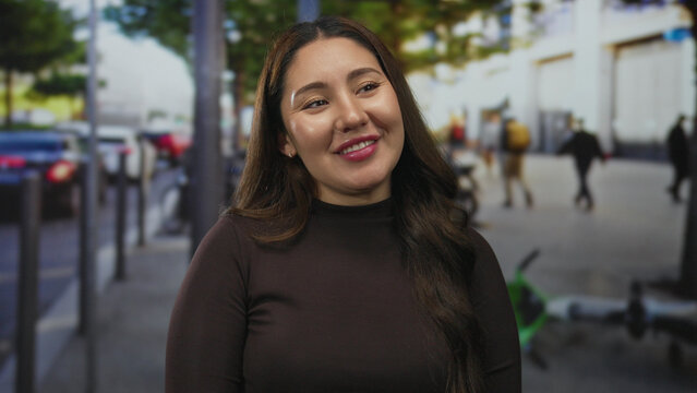 Hispanic woman offers a gentle smile on a busy urban street lined with parked scooters and blurred pedestrians; serenity.