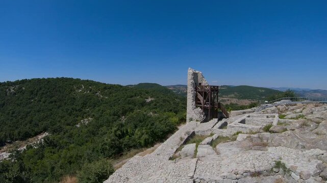 Low drone flight rotating around the ancient Perperikon complex in the Eastern Rhodopes, revealing rocky terraces, stone walls and the acropolis under bright summer light