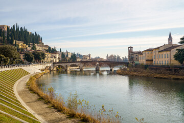 A Adige river in Verona Italy with a bridge and a town in the background. The water is calm and the sky is cloudy