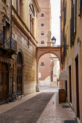An old street with a statue on it in the city of Verona, Italy On the right building there is a lantern with an iron holder, on the left side there are a couple of bicycles parked